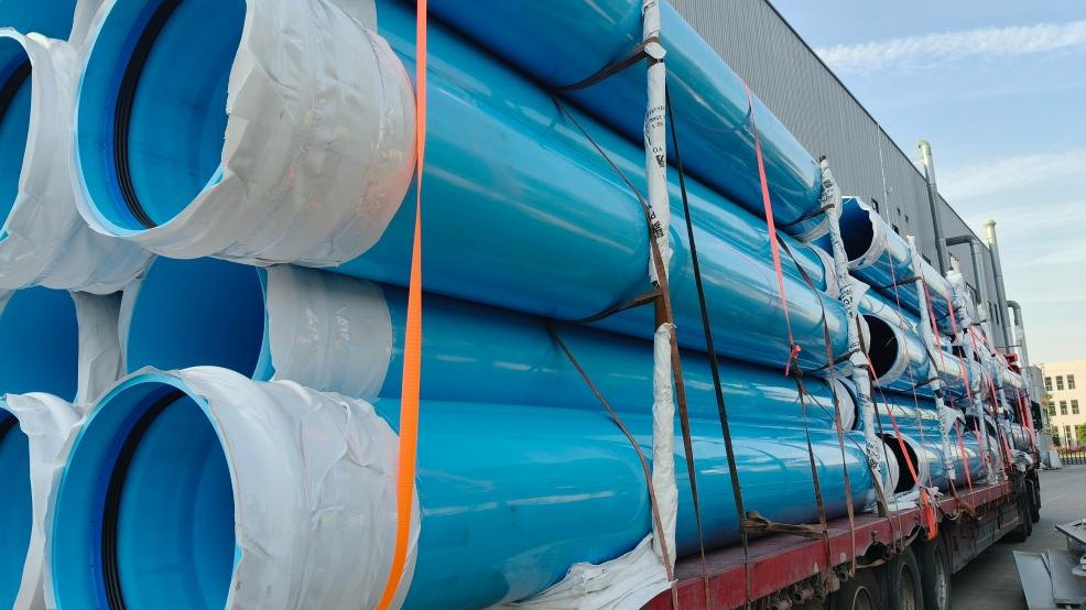 PVC-O给水管装车近景,橙色紧绳器与绑带分段紧固,管口用保护膜包裹